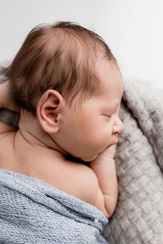 Sleeping newborn baby wrapped in a soft blue knit blanket with dark hair visible.