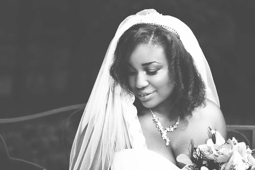 Black and white portrait of a bride in a white veil and gown holding a bouquet, looking down gracefully. At Oaks farm wedding venue.