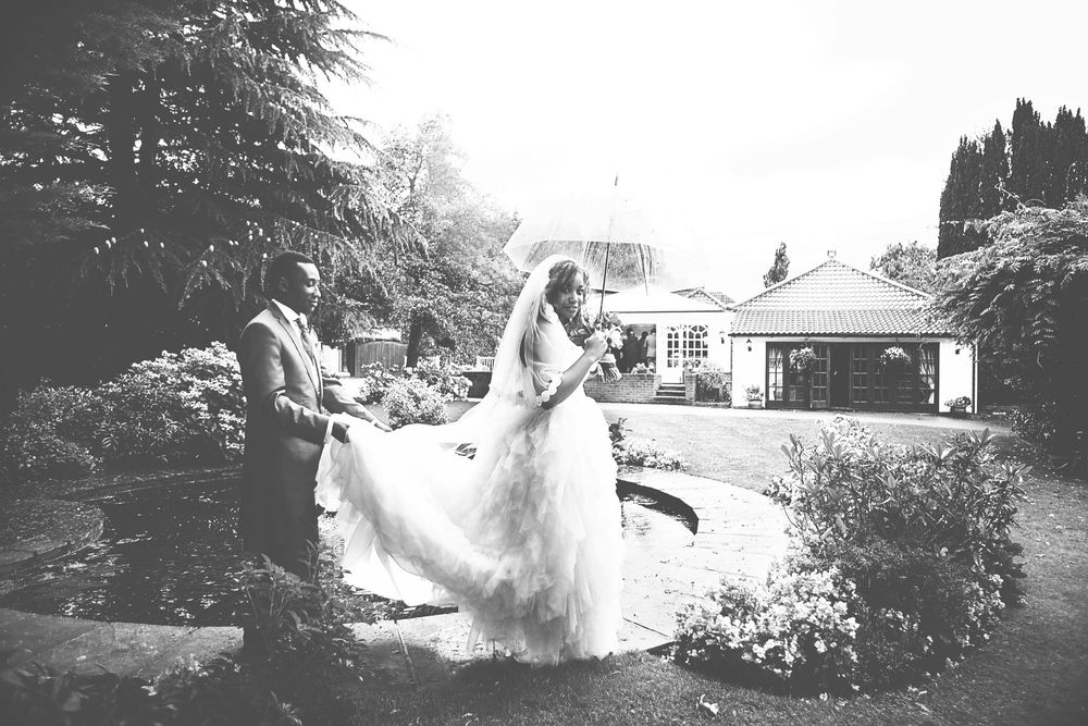 Black and white wedding photo of bride and groom in a garden setting with a house in the background. At Oaks farm wedding venue in Surrey.