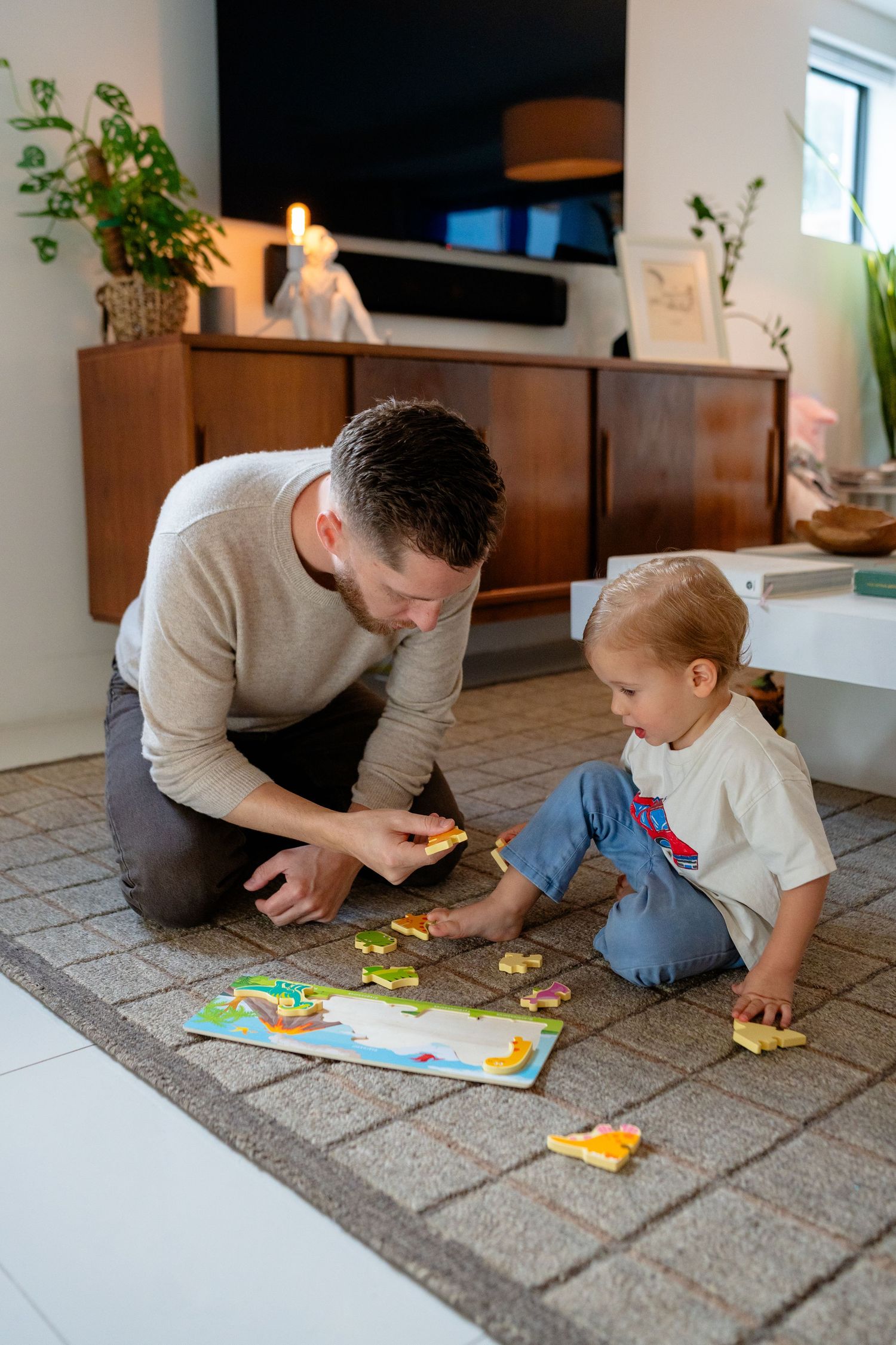 Father holding toddler while pointing at a vinyl record on a turntable in a bright home music room.