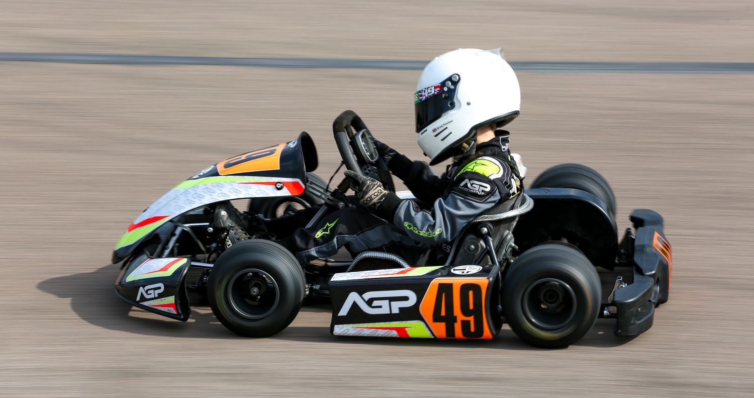 Young driver in white helmet racing black AGP go-kart number 49 on a track.