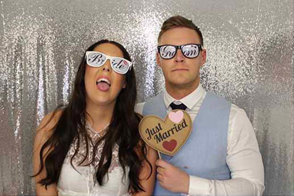 Newlywed couple posing in a photo booth wearing Mr and Mrs glasses holding a Just Married heart sign at New House Farm wedding reception