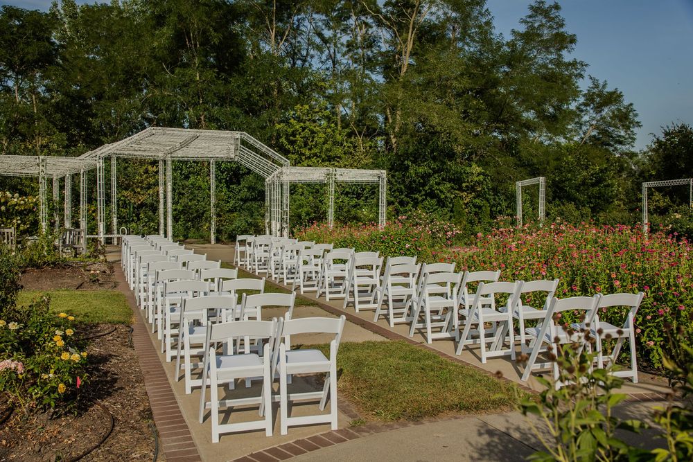 White folding chairs arranged in rows for an outdoor wedding ceremony in a lush garden with pergolas.