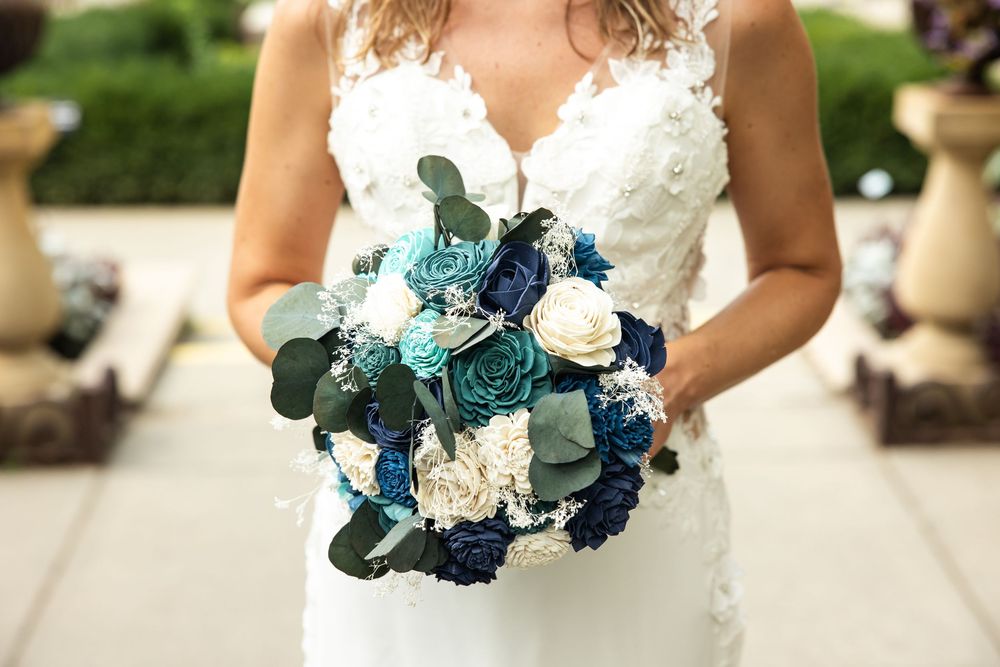 Bride in lace wedding gown holding a bouquet of teal, navy, and white flowers with eucalyptus greenery.