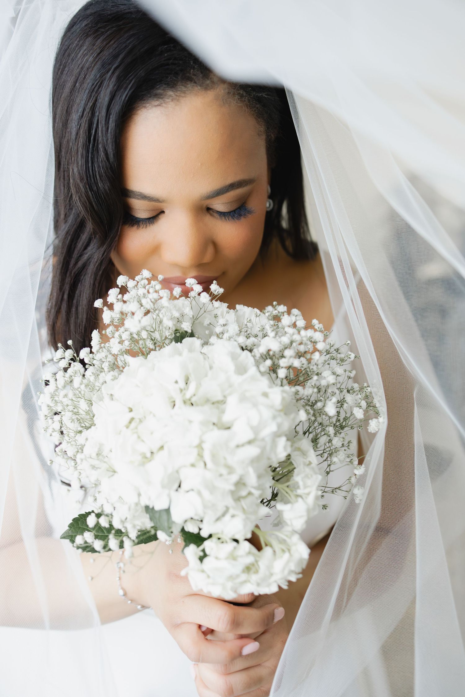 Bride in white veil smelling a bouquet of white hydrangeas and baby's breath on her wedding day.