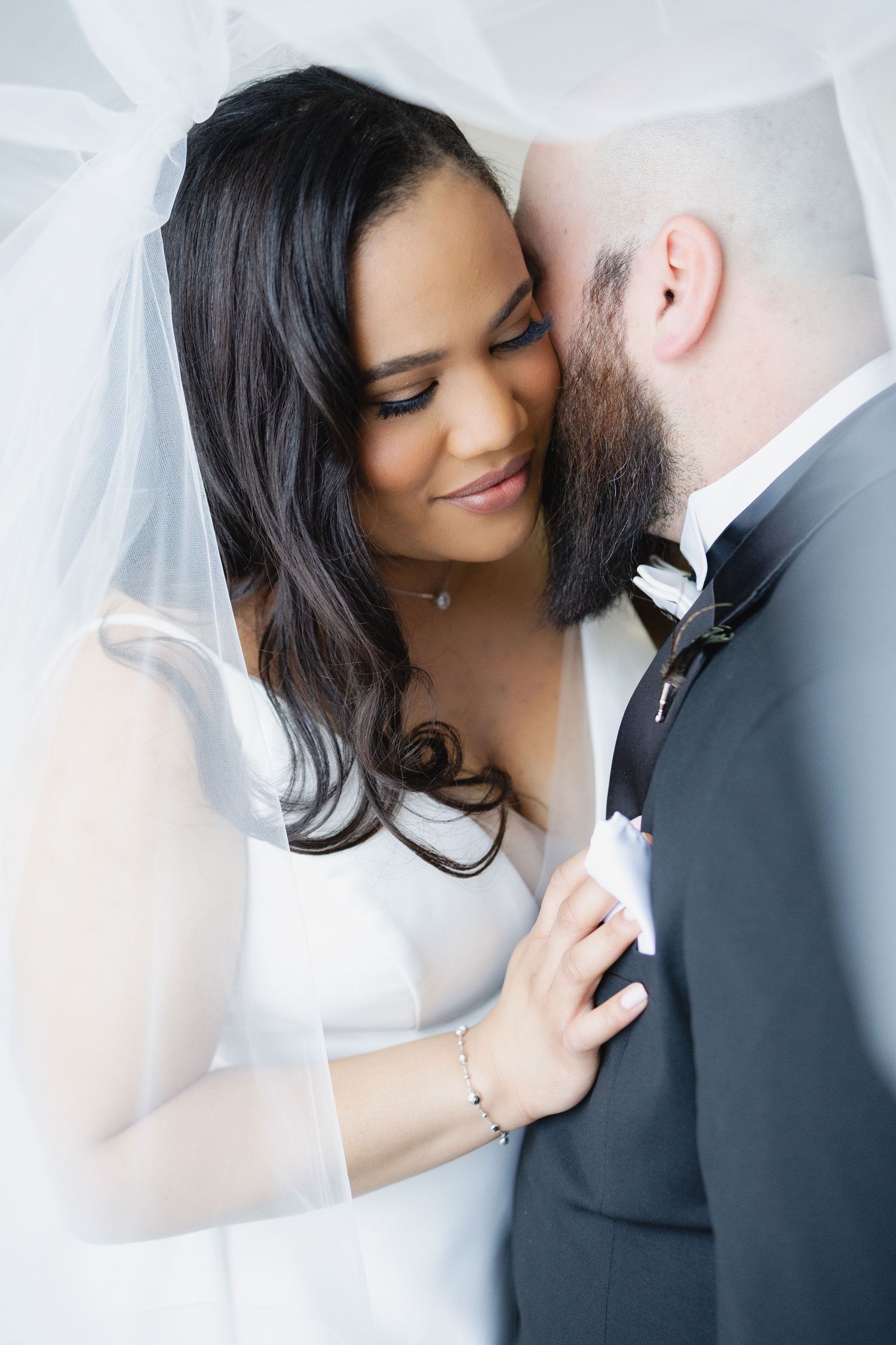 Bride and groom share an intimate moment under a white veil on their wedding day.