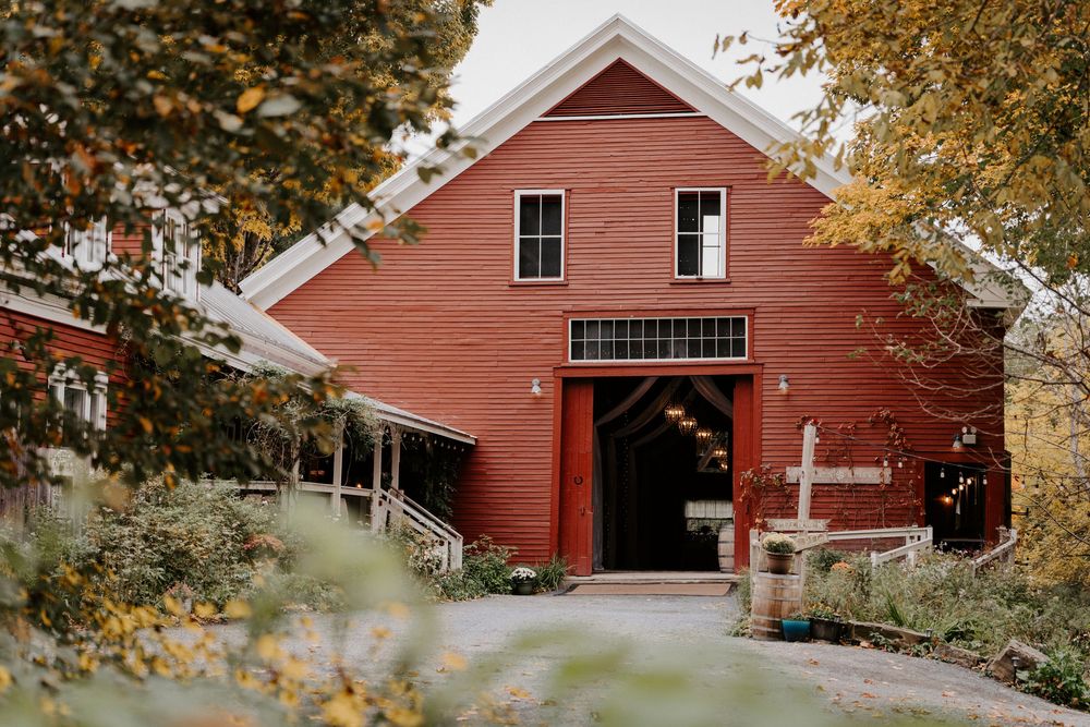 Red barn wedding venue surrounded by autumn foliage and lush greenery, featuring rustic charm and elegant white trim details.