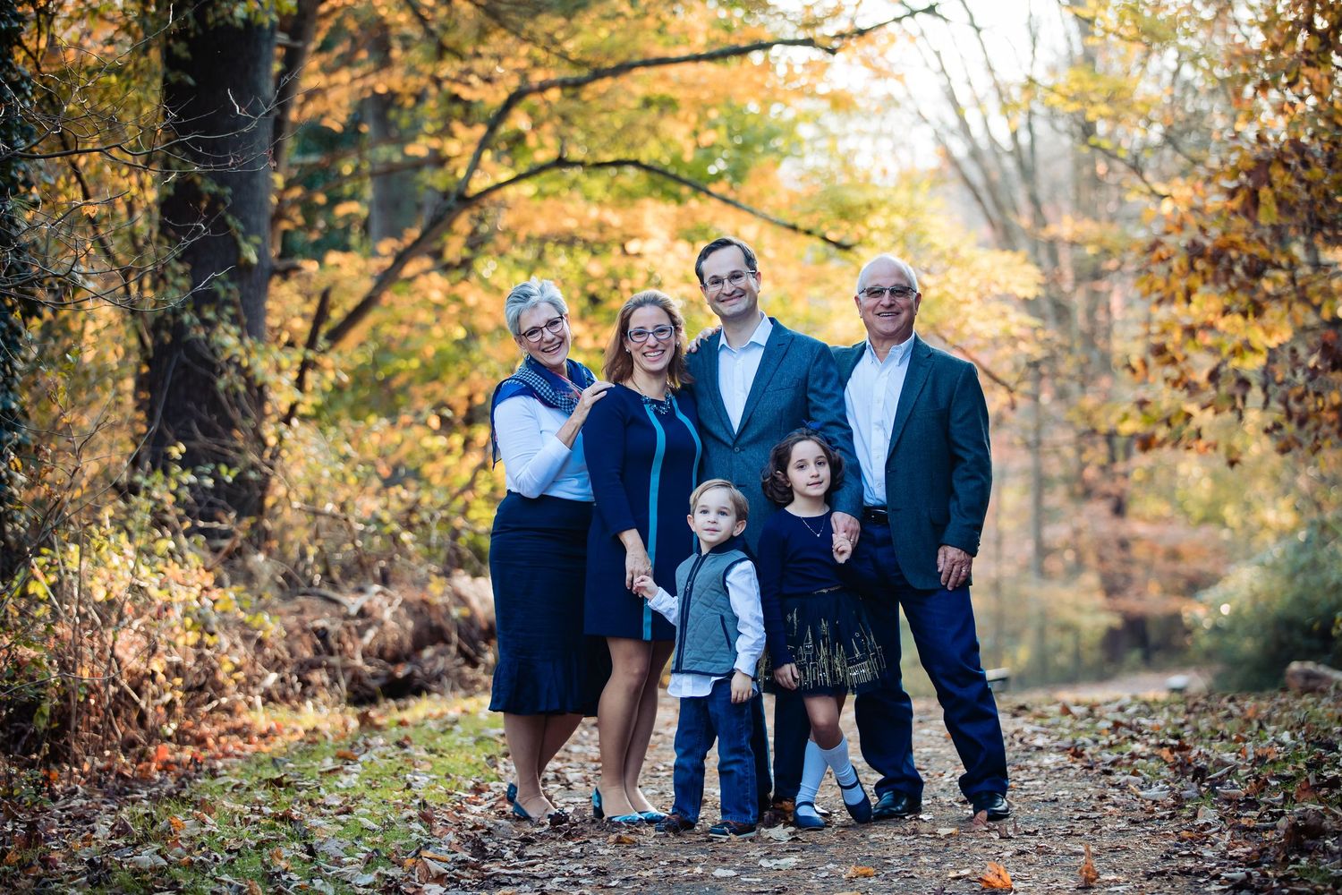 Family of seven posing on a forest path surrounded by colorful autumn foliage for a fall portrait.