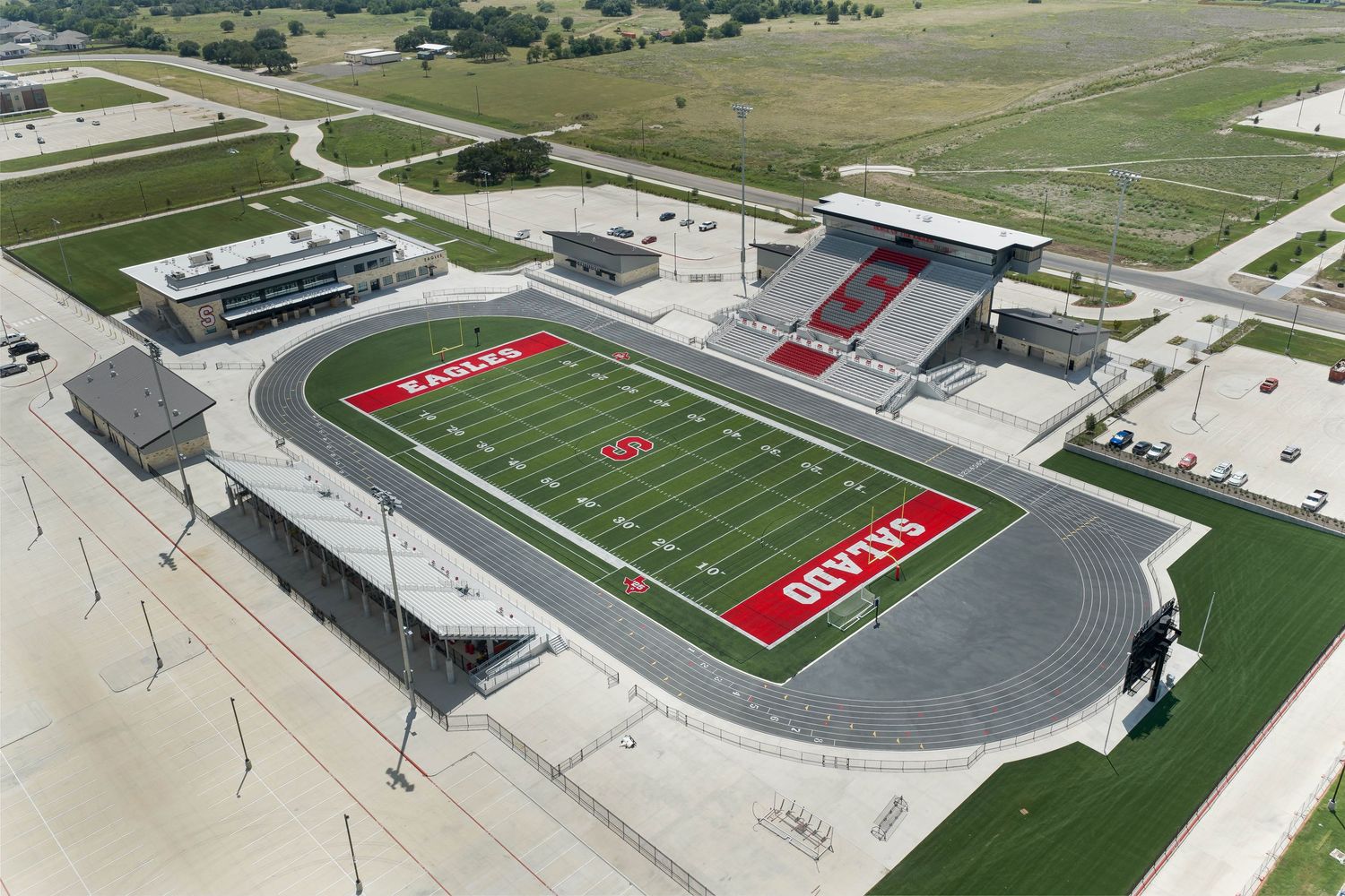 Aerial view of Salado Eagles high school football stadium with red turf markings, modern grandstands, and surrounding green fields.