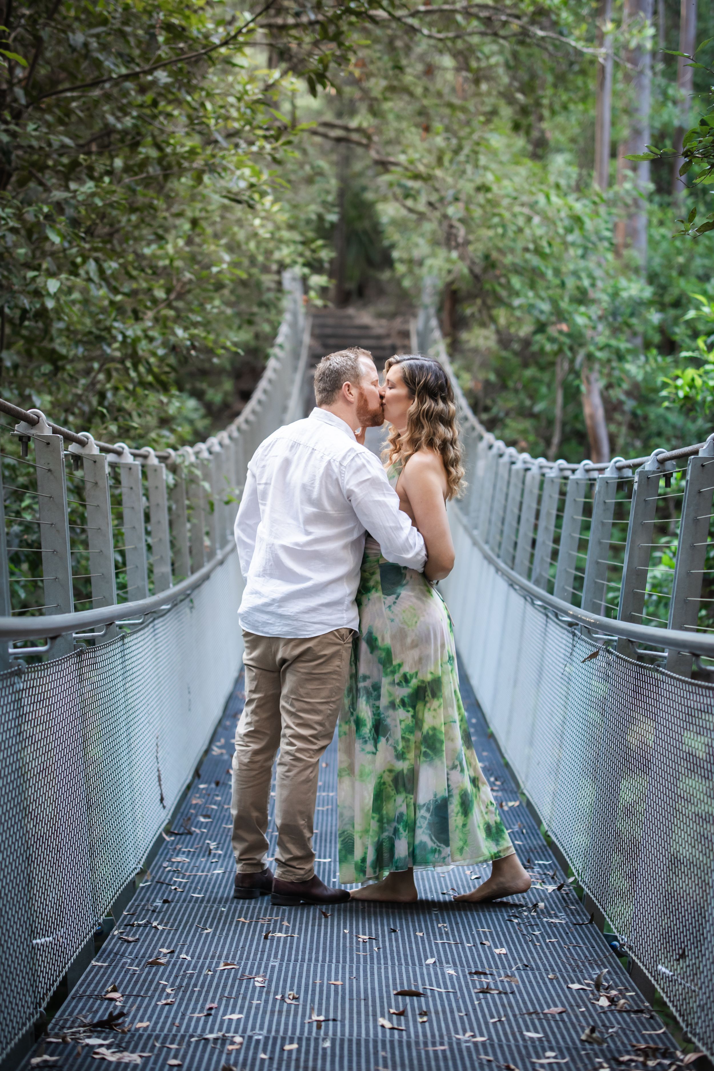 Couple sharing a kiss on The Swing bridge in Cherrybrook surrounded by lush green forest trees.