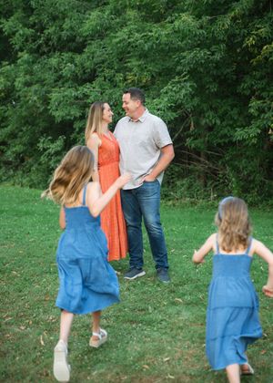 A family of four with two girls in blue dresses running toward their parents on a green lawn.