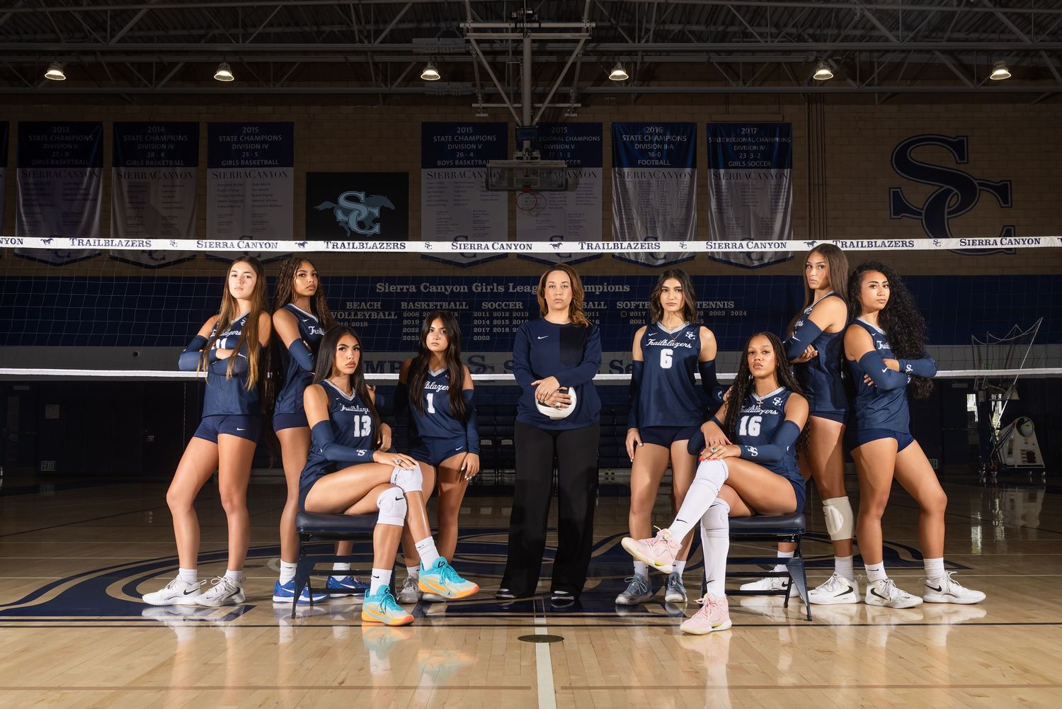 College volleyball team poses in navy uniforms on indoor court with SC logo backdrop for official team photo.