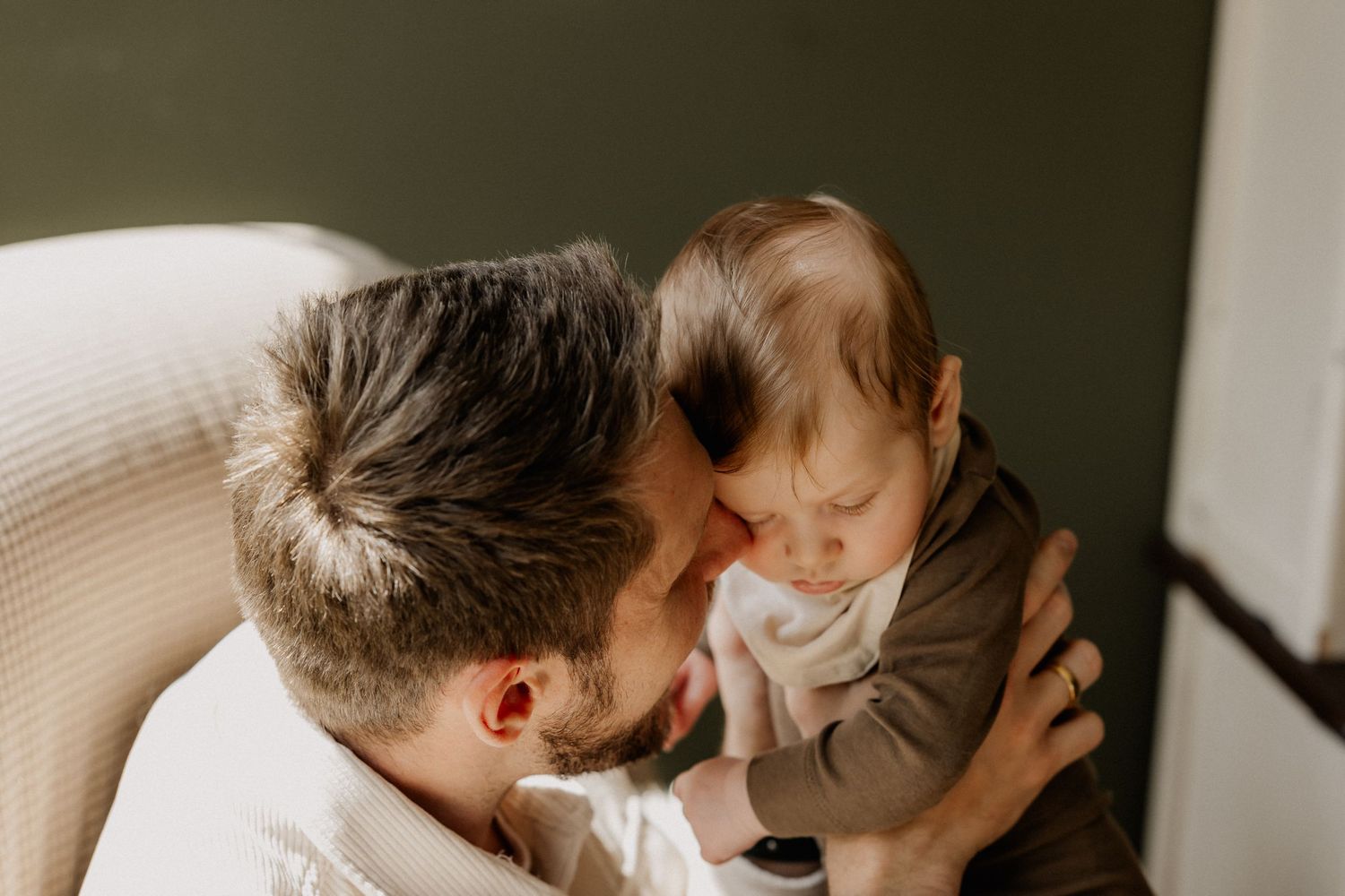 A father tenderly nuzzles his newborn baby, sharing a sweet bonding moment in a softly lit room.
