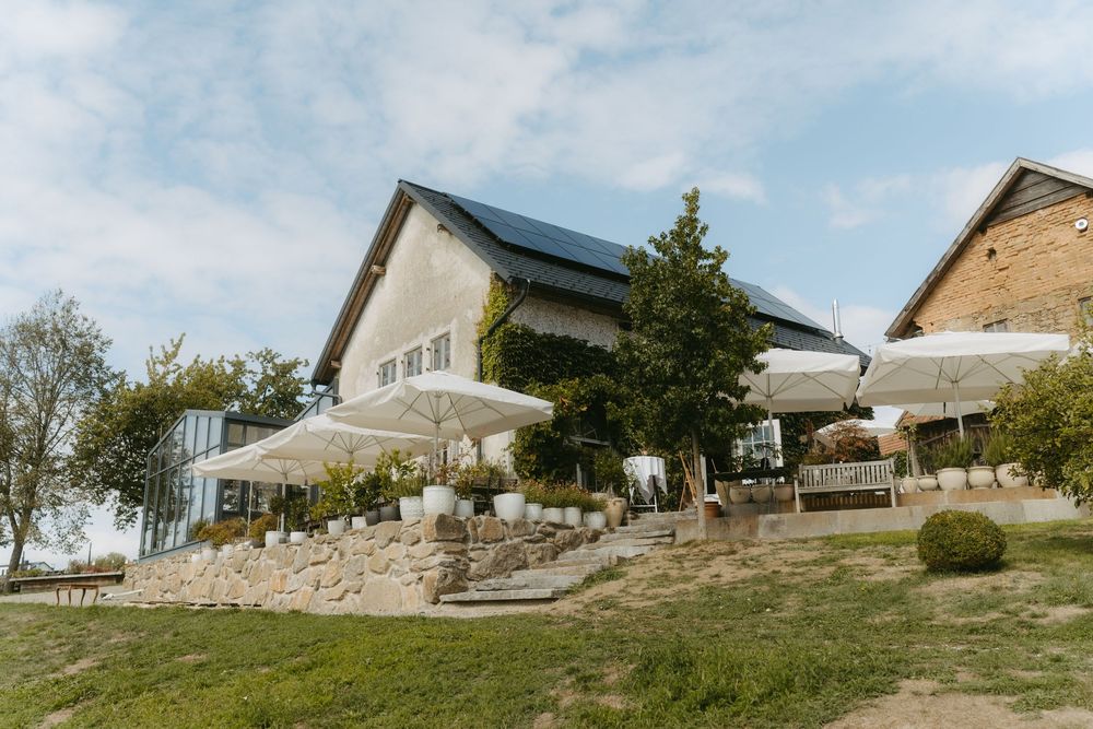 Elegant wedding venue exterior with white umbrellas, stone terrace, and modern building under a blue sky.