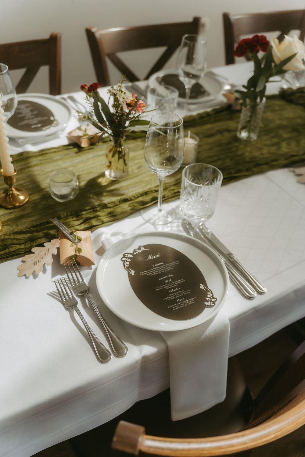 Sophisticated wedding table setting with dark menu card, white plates, crystal glasses, and floral centerpieces.