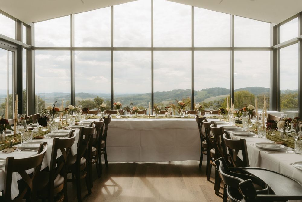 Bright wedding reception room with large windows, scenic valley views, white tablecloths, and floral centerpieces.