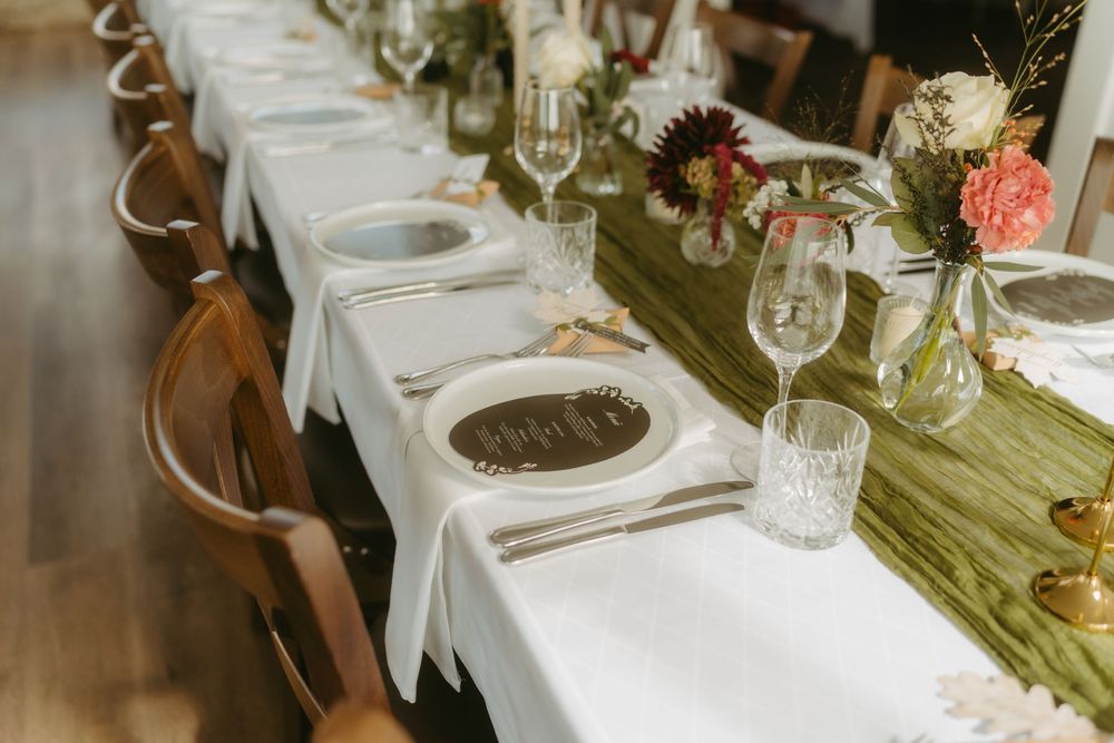 Elegant wedding reception table set with white linens, floral centerpieces, wine glasses, and wooden cross-back chairs.