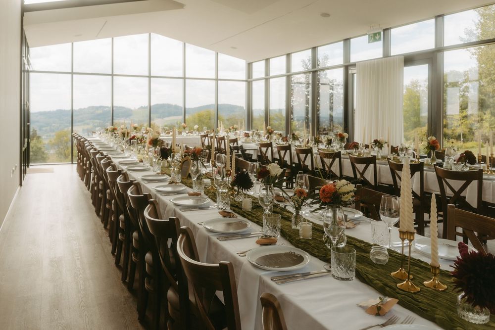 Elegant wedding reception hall with long tables, floral centerpieces, candles, and panoramic floor-to-ceiling windows.