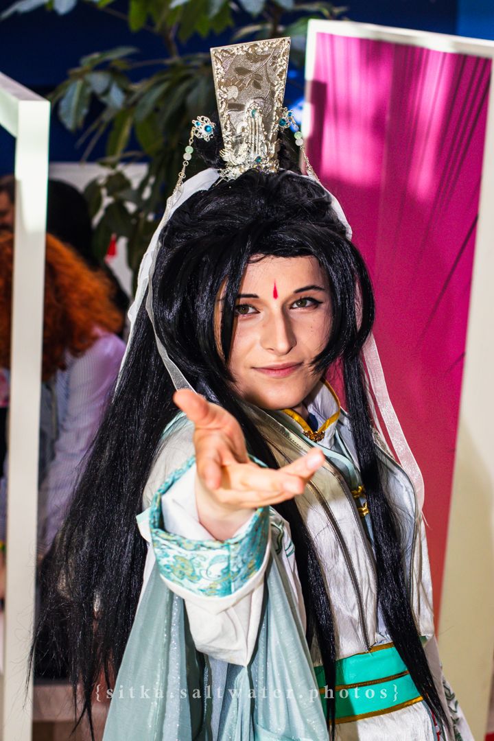 Person cosplaying as an Asian fantasy character with black wig, silver crown, red bindi, and teal hanfu costume reaching toward camera.