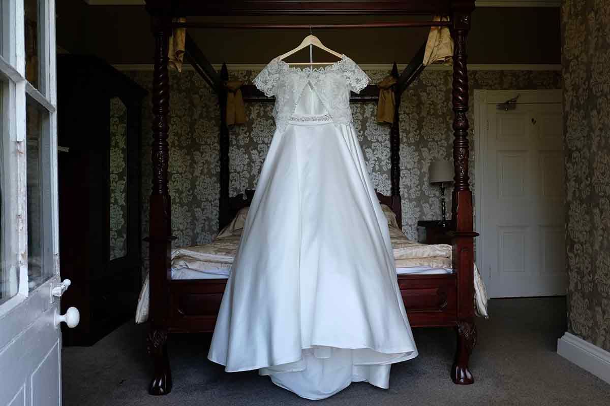 White wedding dress with lace bodice hanging on a four-poster bed in the bridal suite at Blaithwaite House wedding venue