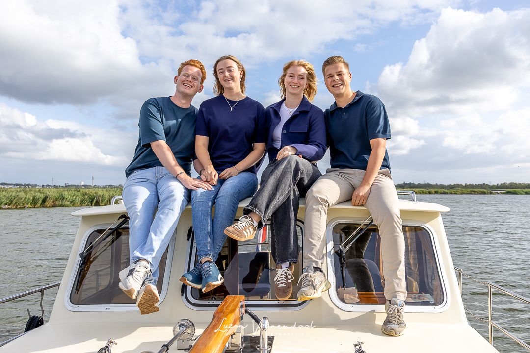 Zoon en dochter met partners zitten samen op het dak van de boot, met de polder op de achtergrond tijdens een familiefotoshoot in Uitgeest
