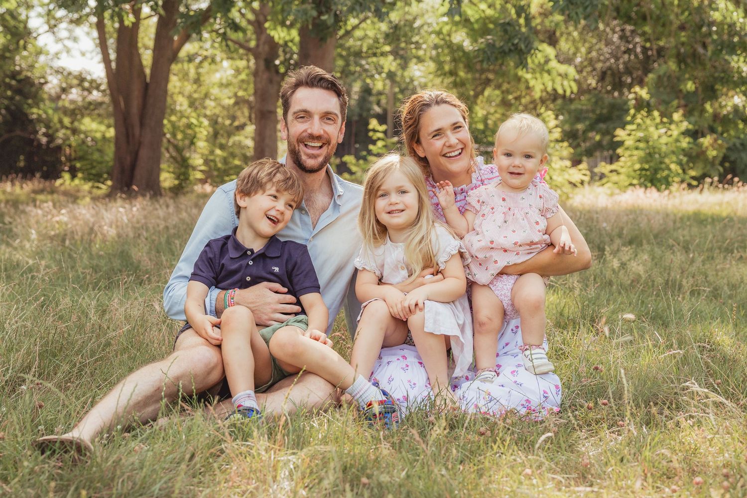 family of four with dog walk away from camera between trees on Wandsworth common
