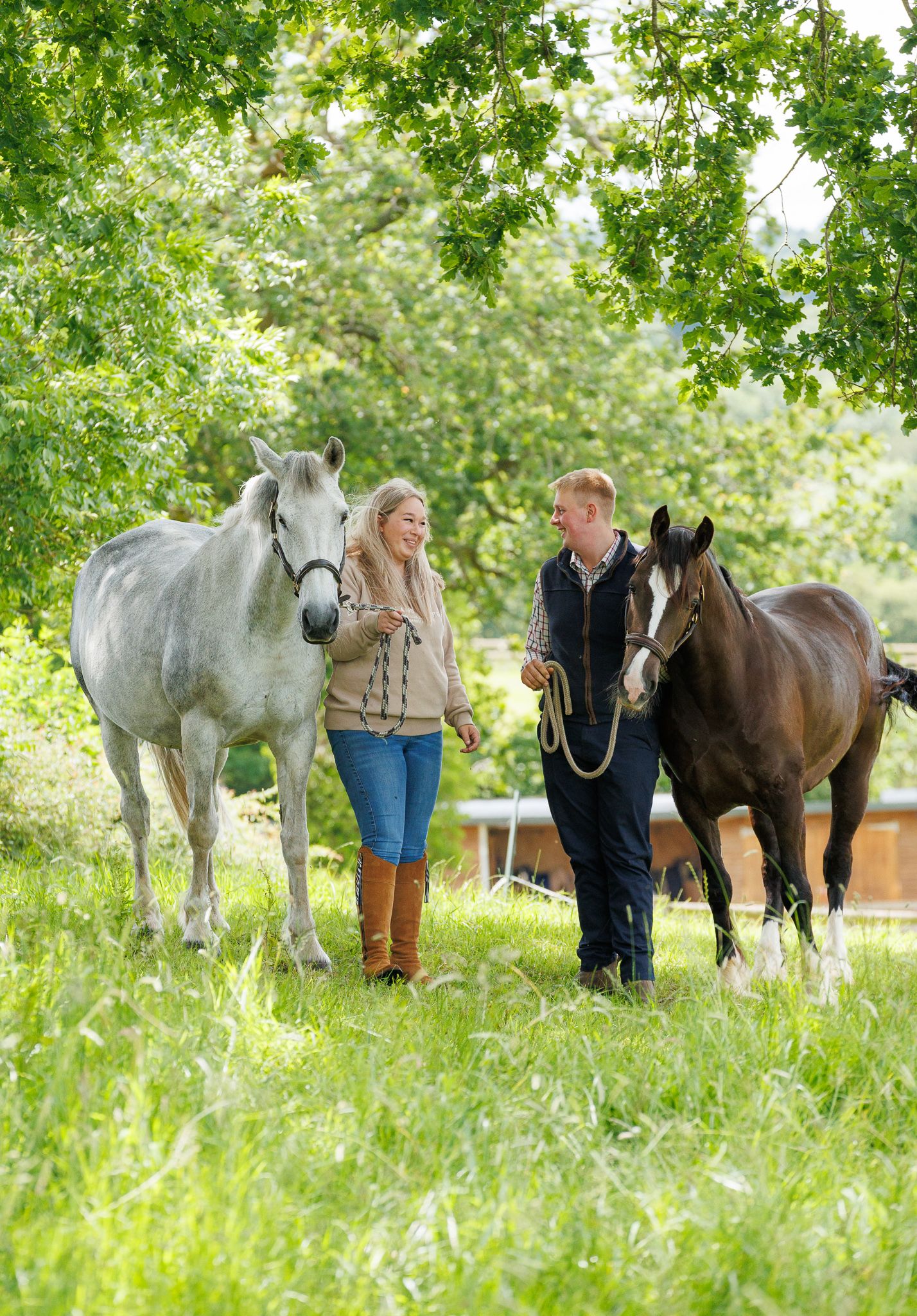 A smiling couple stands with a black and white horse and small dog in front of a white van on a farm.