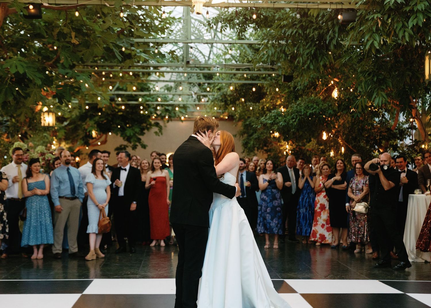 Couple performs wedding dance sequence showing bride dipping backwards in flowing white dress with guests watching and smiling.