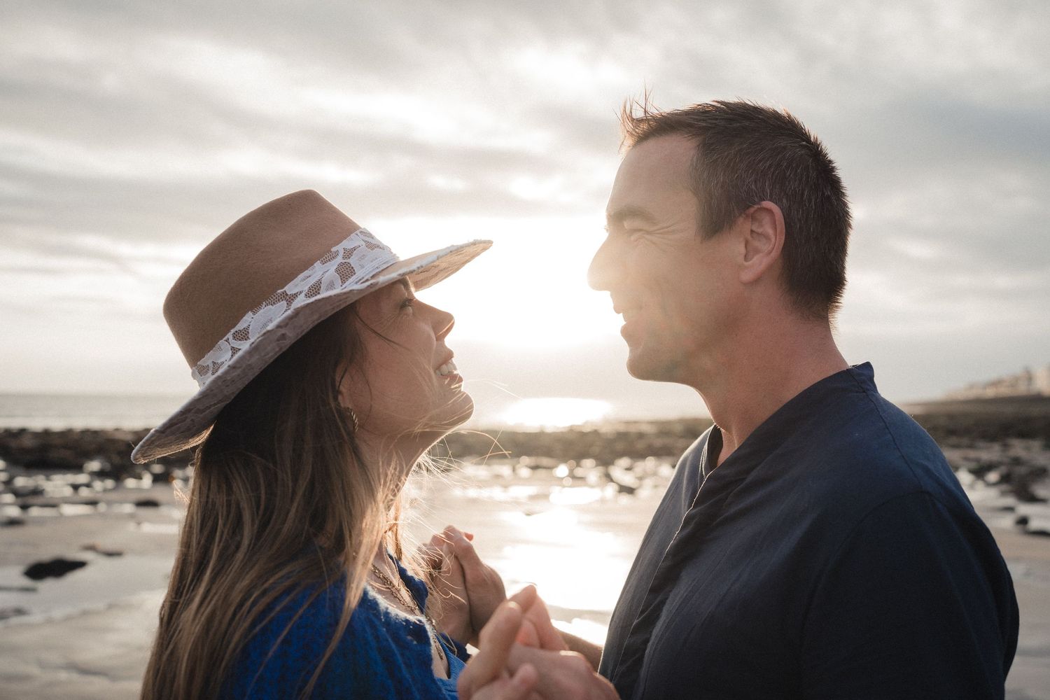 Romantic couple holding hands and gazing at each other on a beach at golden sunset hour.