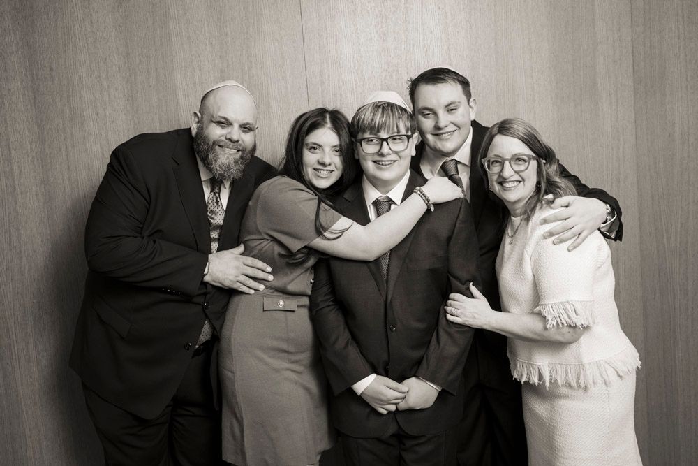 Five people pose together smiling in formal attire against wood-paneled wall in black and white group photo.