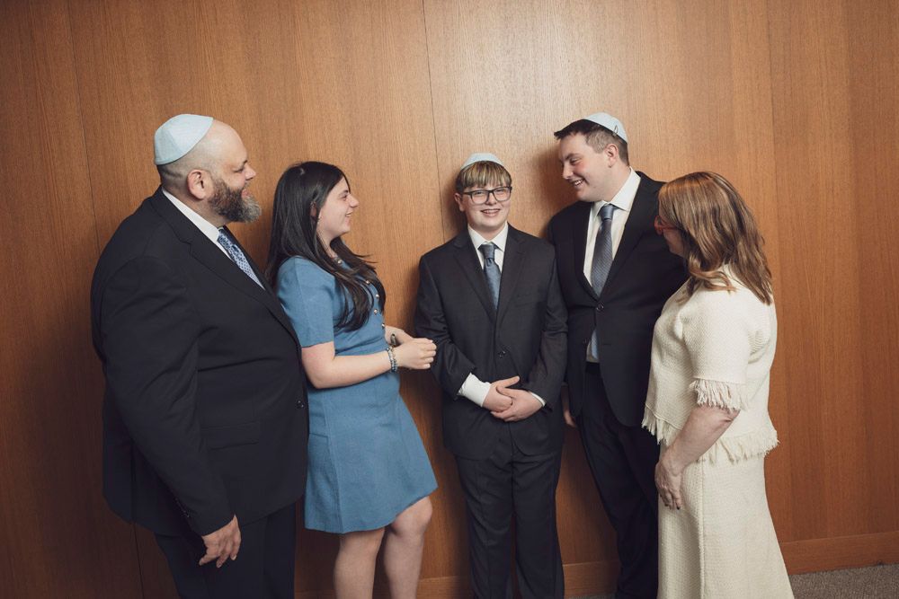 Family gathering in formal attire with yarmulkes at a Bar Mitzvah celebration near a wooden wall.
