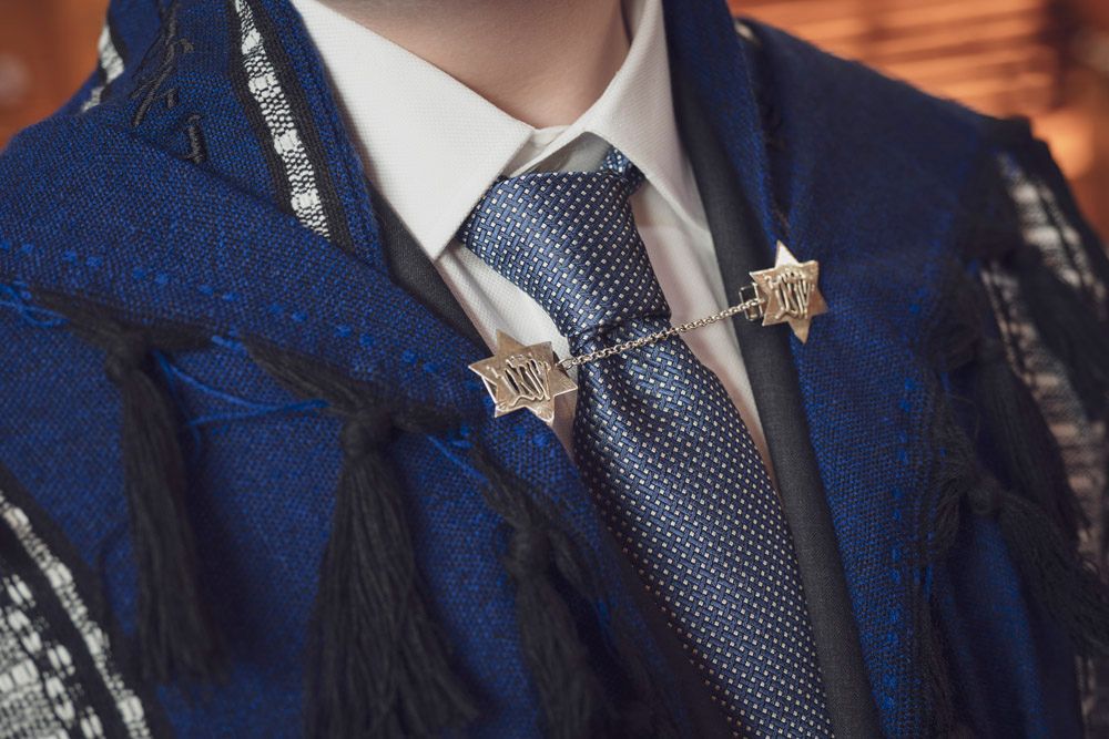 Close-up of a man wearing a blue suit with a star-shaped tie bar and tassel accents on a formal occasion.