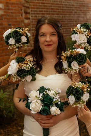 Bride holding green and white rose bouquet surrounded by bridesmaids bouquets at wedding.
