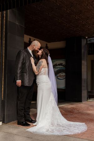 Bride and groom share a kiss outside a hotel entrance, bride wearing lace wedding dress with veil.
