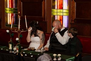 Bride and groom sharing emotional moment at wedding reception table with stained glass windows.