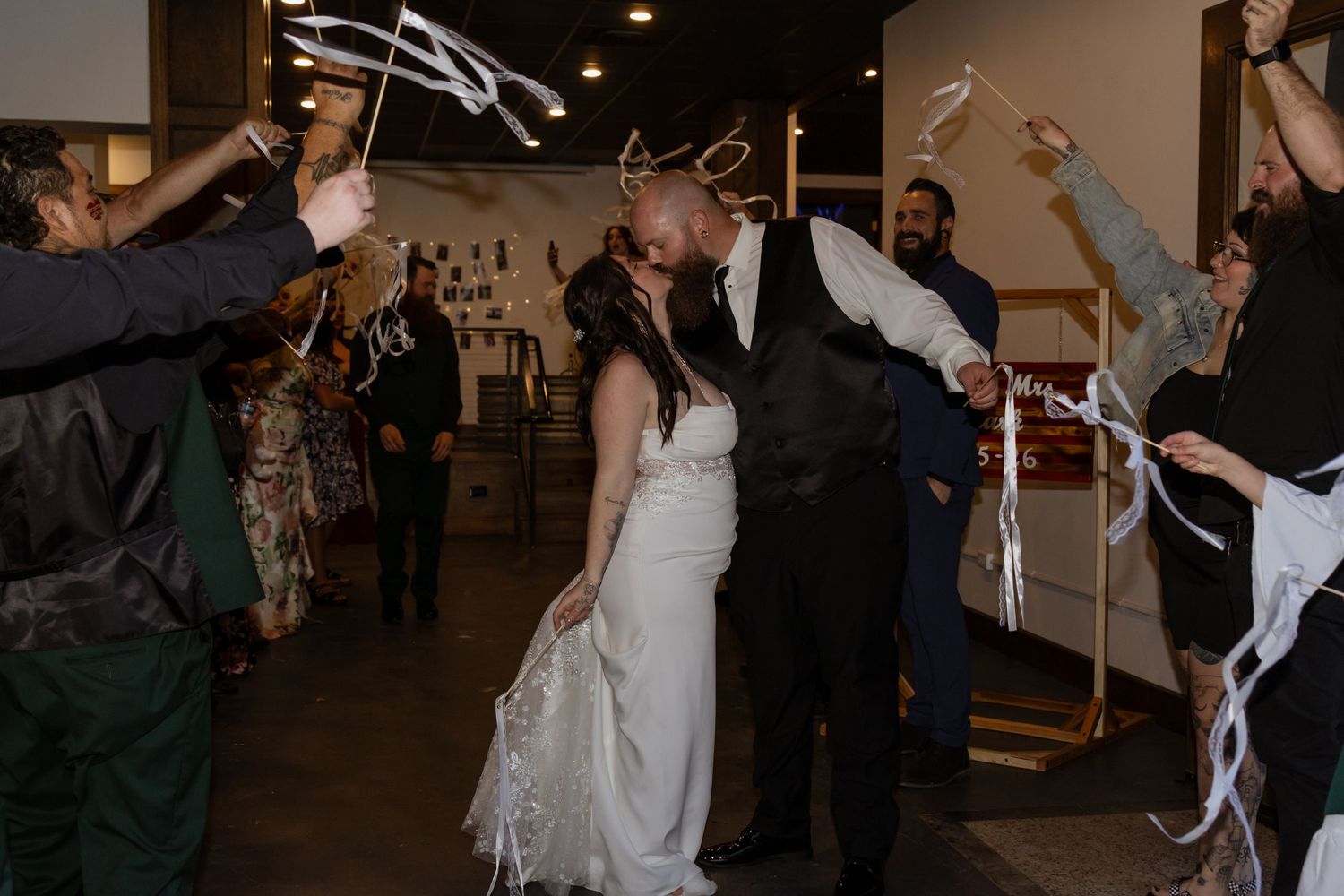 Bride and groom share a kiss during sparkler send-off exit at wedding reception with guests celebrating around them.