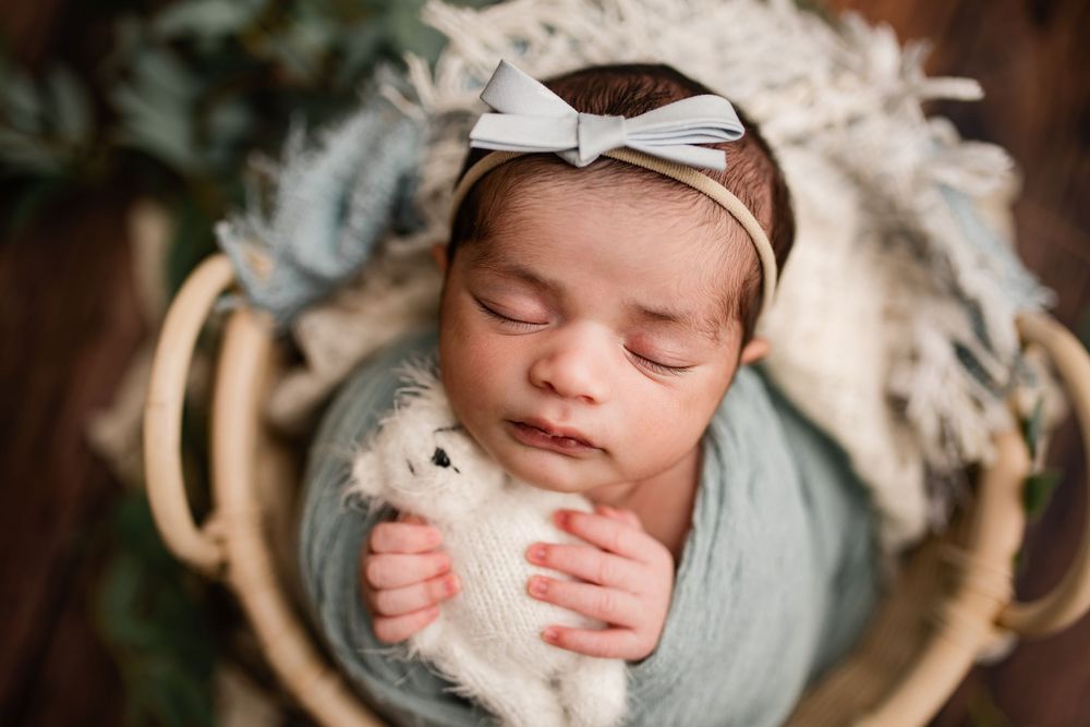 Sleeping newborn baby wrapped in blue holding a stuffed bunny in a wicker basket.