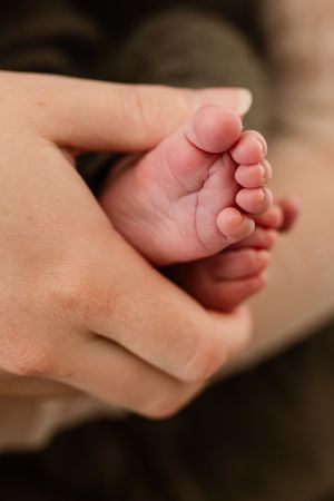An adult hand gently cradling a tiny newborn baby foot, showcasing the delicate size difference between parent and child.