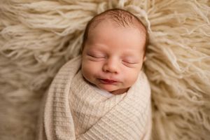 Peaceful sleeping newborn baby swaddled in cream wrap on fluffy beige fur backdrop.