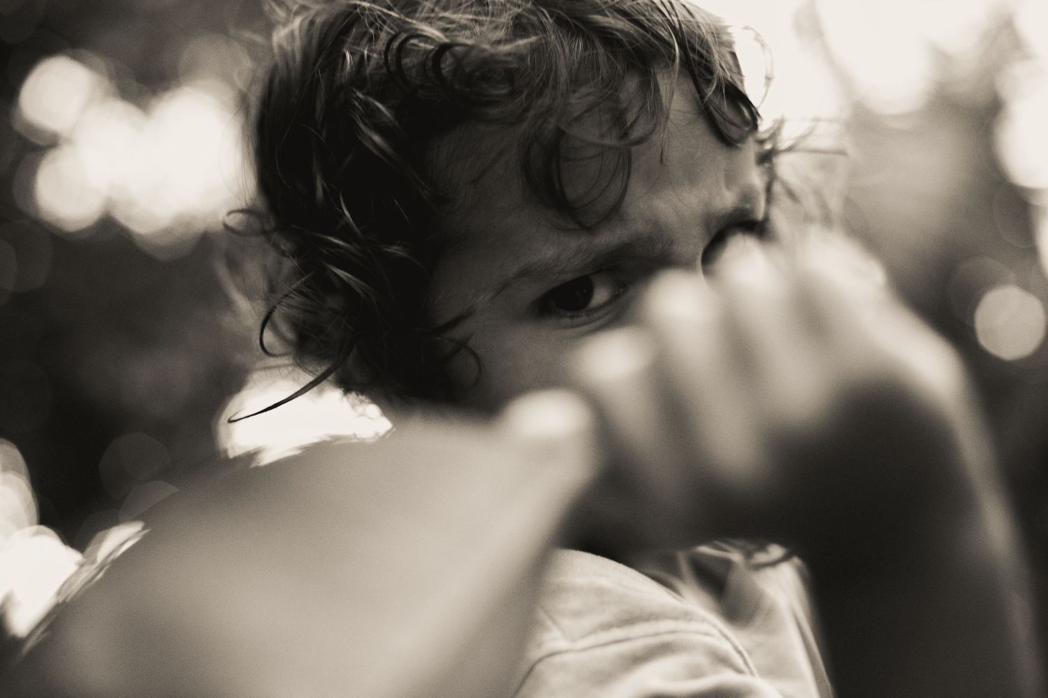 Black and white photo of a child holding a large leaf over their face, arms raised above their head.