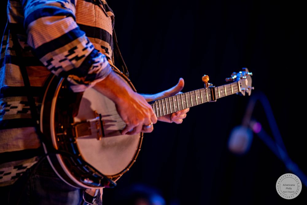 Close-up of a musician playing a banjo on stage under blue concert lighting.
