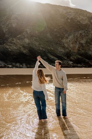 Couple dancing in shallow water on a sunlit beach with mountain behind them.