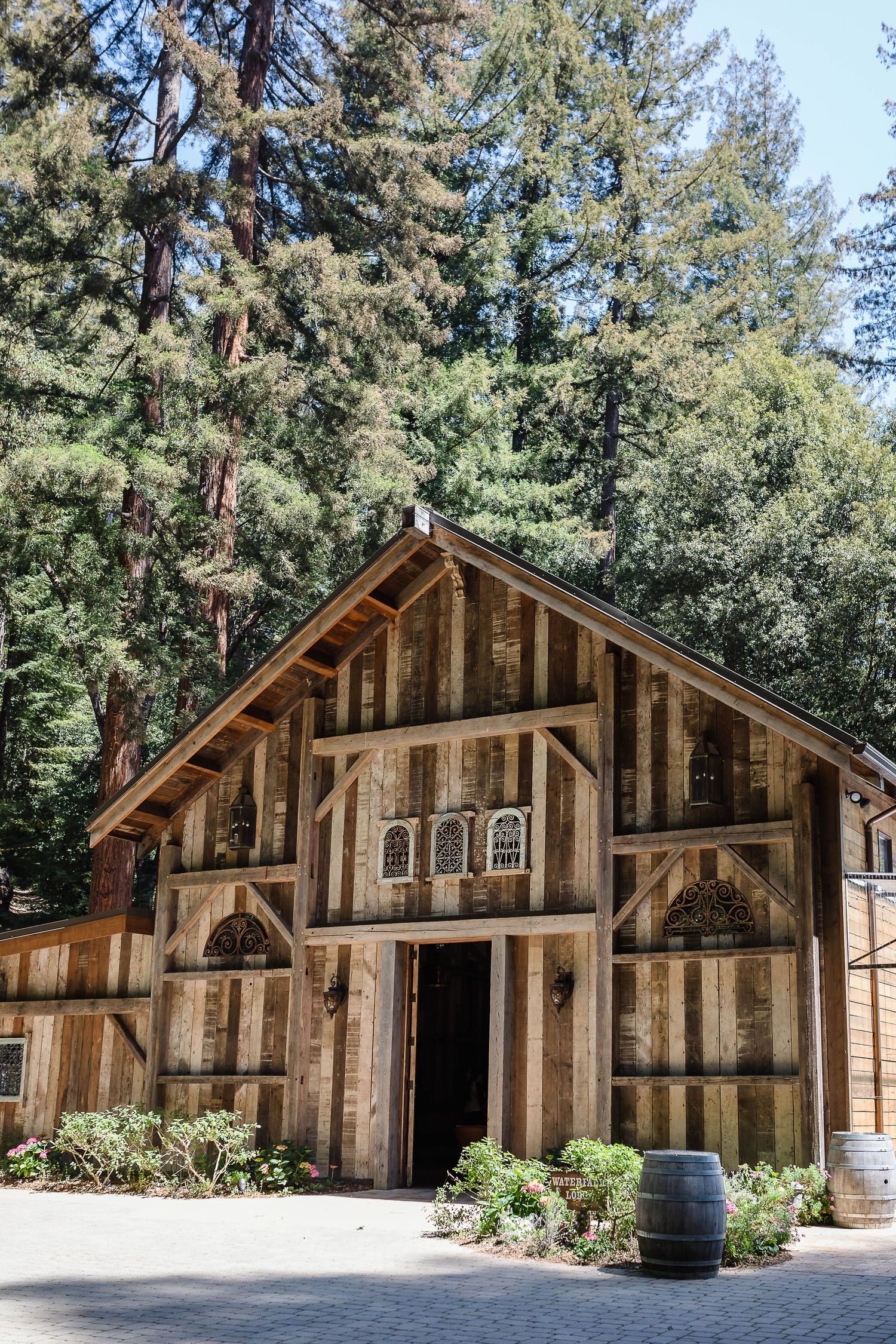 Outdoor wedding ceremony setup with white chairs, brick aisle, wooden floral arch, and towering redwood trees in a forest.