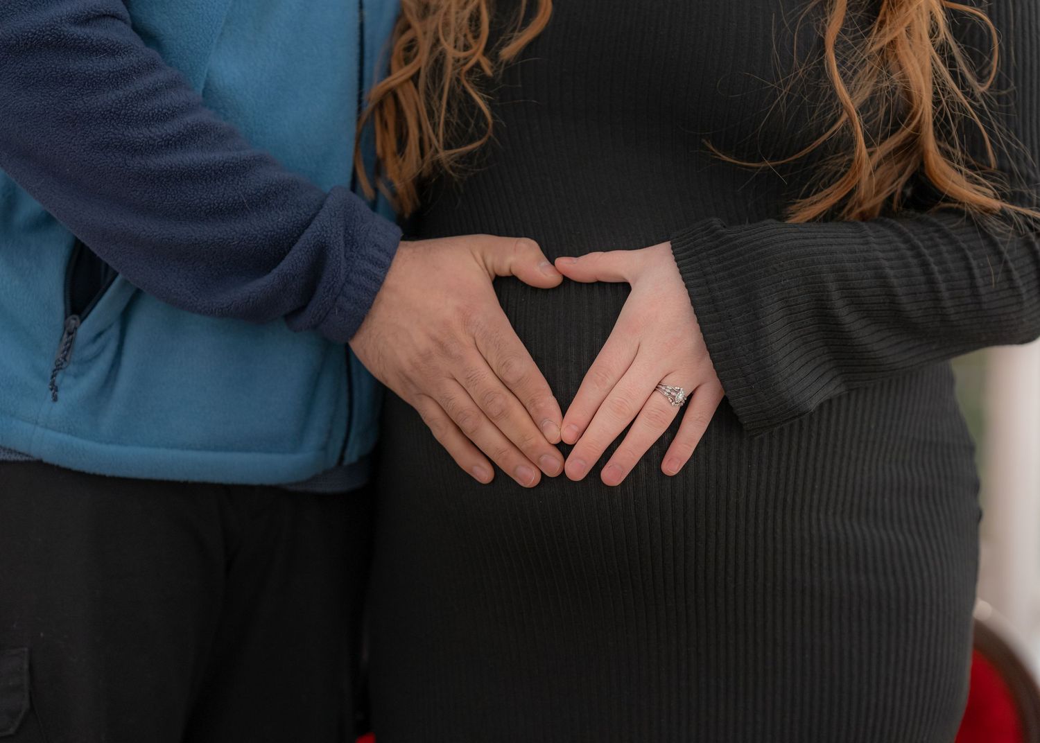 Couple forming a heart shape with hands on pregnant belly, maternity photo shoot.