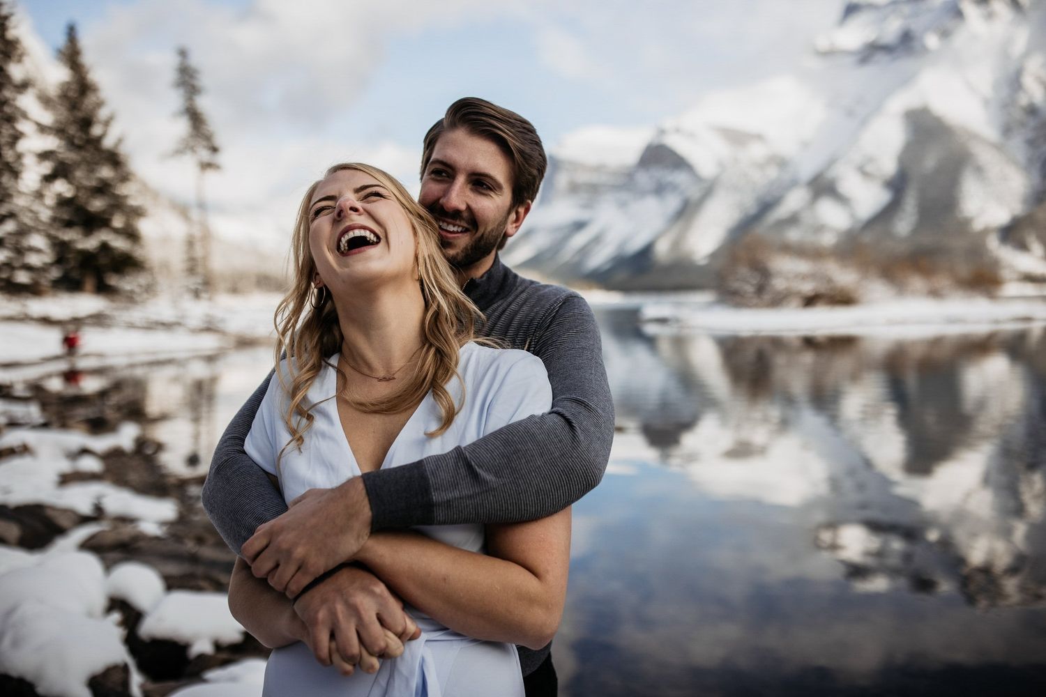 Laughing bride wrapped in a hug with snowy mountains and a lake behind, by a Lake Louise wedding photographer