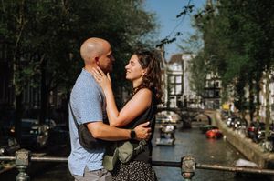 Couple embracing romantically on a bridge over an Amsterdam canal on a sunny day.