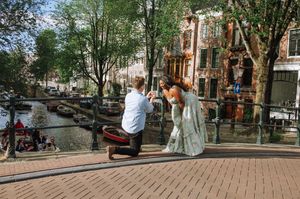 Man proposing to woman on a bridge in Amsterdam with canal and historic buildings in the background.