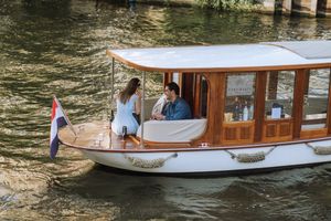 Couple enjoying a scenic canal boat ride on a classic wooden vessel flying a Dutch flag.