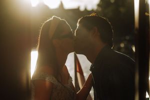 Romantic couple sharing a kiss backlit by golden sunset light in a warm, intimate outdoor setting.