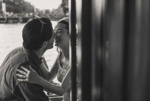 Black and white photo of a romantic couple sharing an intimate moment, leaning close together near a window.